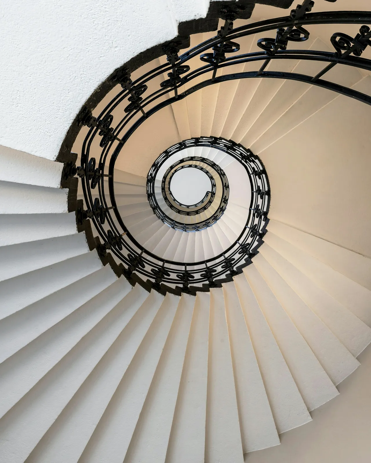 Helles Treppenhaus mit weißer Wendeltreppe und schmiedeeisernem Geländer, von oben aufgenommen