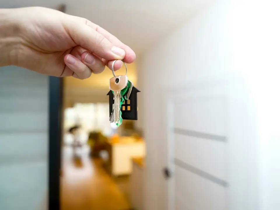 Eine Hand hält einen Wohnungsschlüssel vor einer offenen Wohnungstür