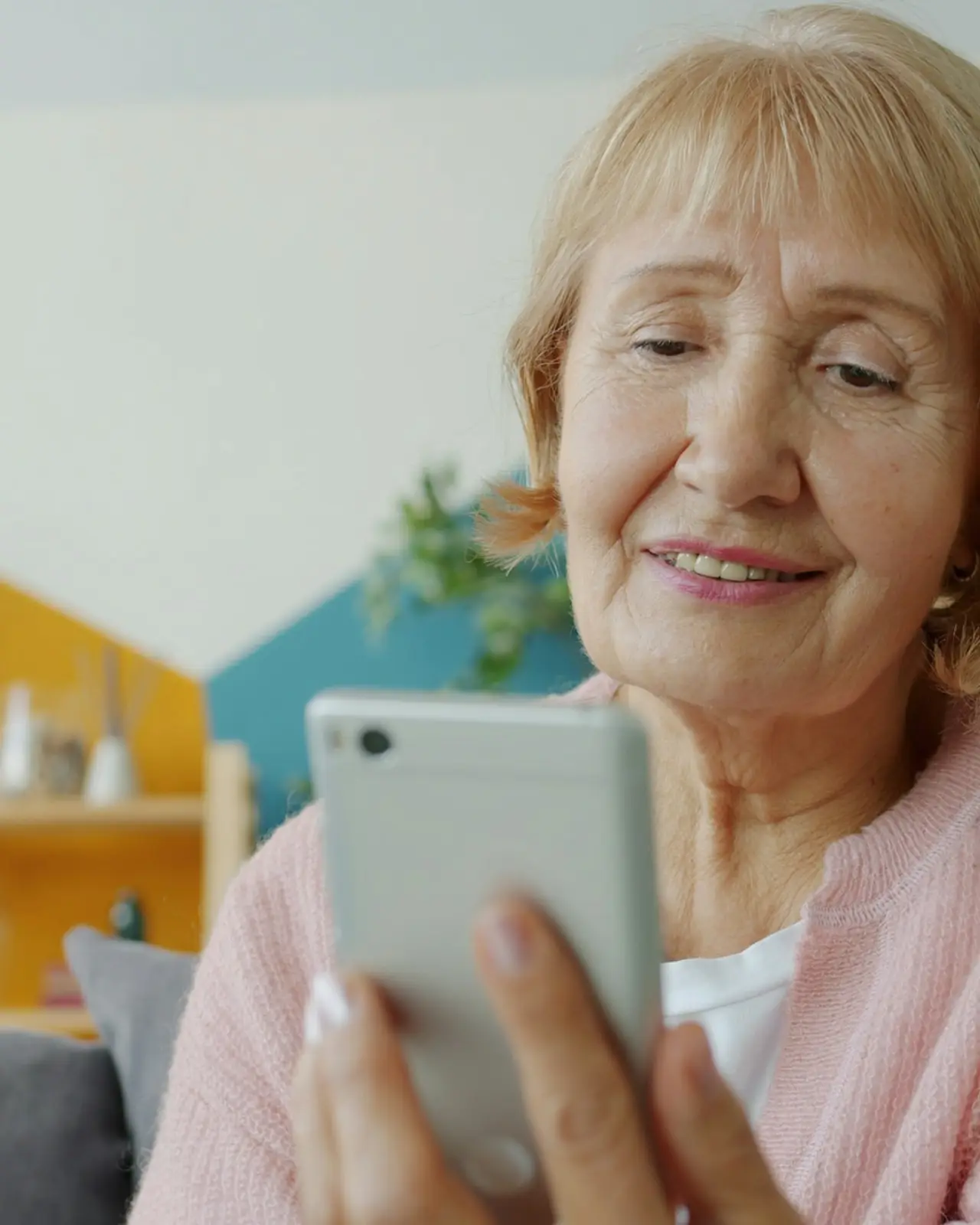 Eine ältere Frau liest lächelnd etwas auf ihrem Telefon