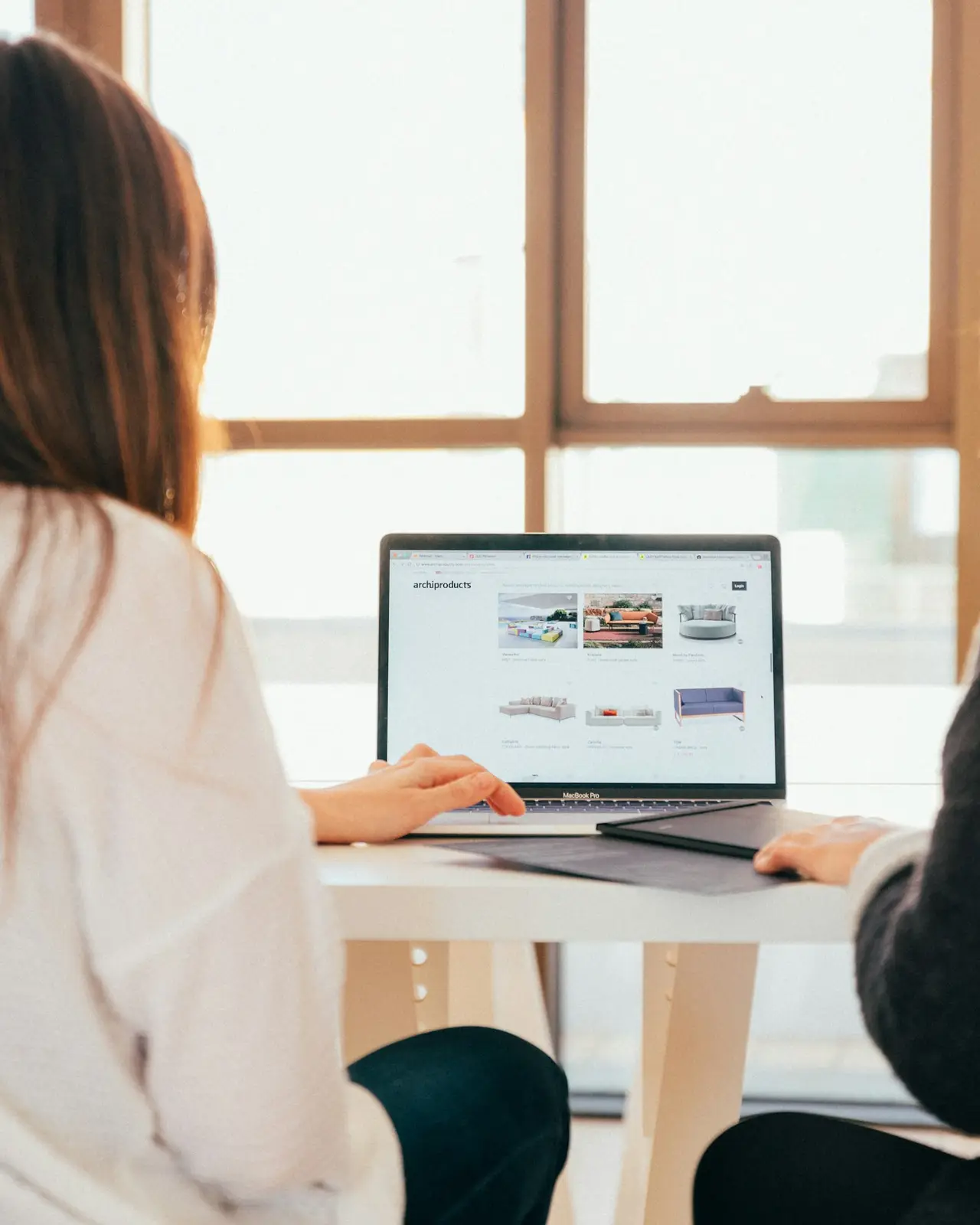 Zwei Personen sitzen vor einem Fenster an einem Laptop und sehen sich gemeinsam eine Website an
